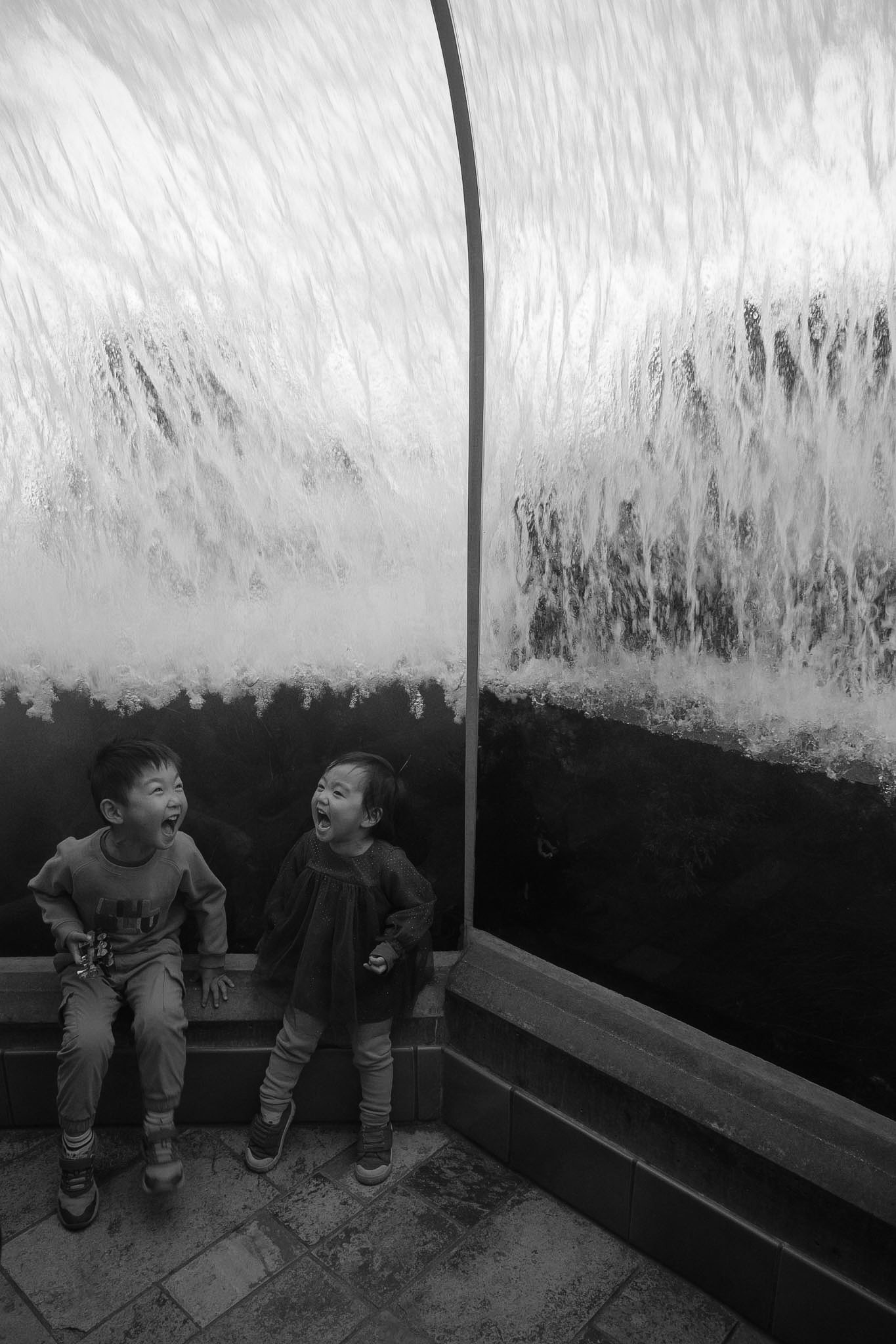 Two children laughing under a waterfall